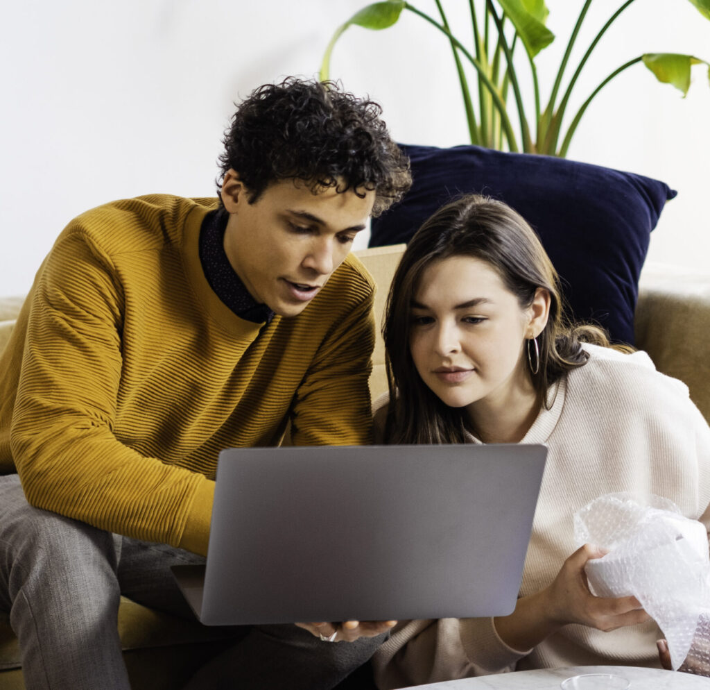 Two people collaborating at a desk with a laptop, discussing marketing or client work in a bright modern office.